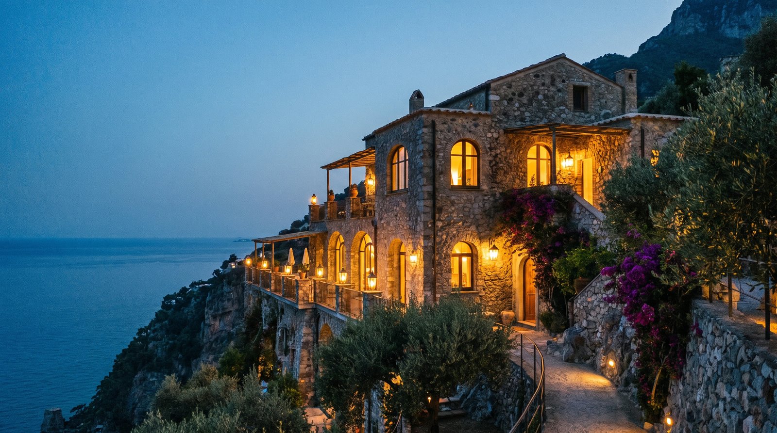 Aurelia Retreat exterior at twilight, warm interior light against cliffside stone architecture.