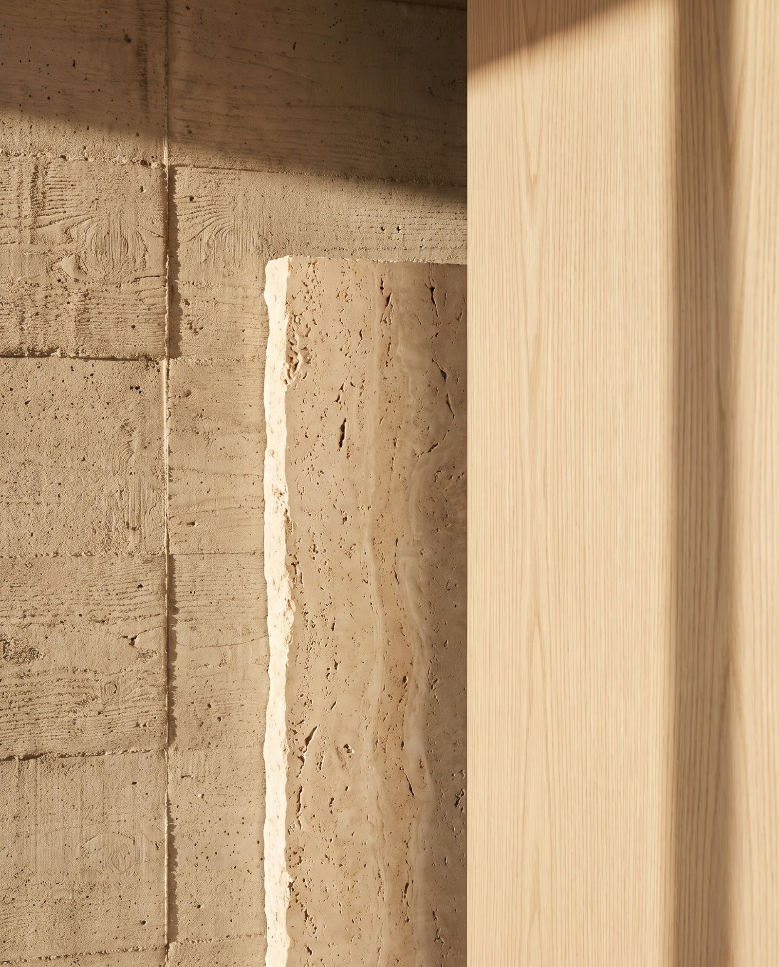 Close-up of board-formed concrete, travertine stone, and oak wood grain in warm raking light.